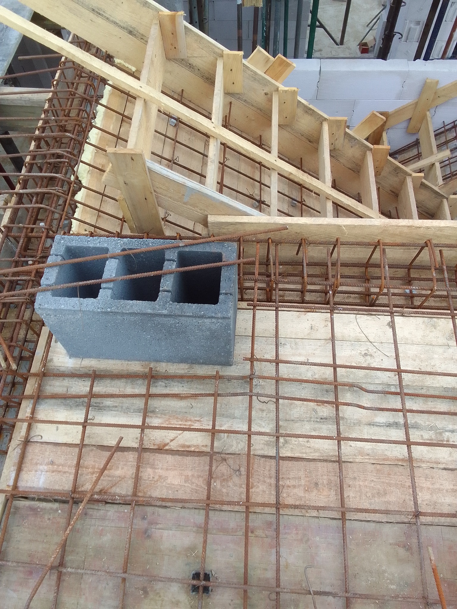 Szary bloczek betonowy na drewnianym szalunku z siatką zbrojeniową, widoczne elementy konstrukcji szkieletowej z drewna.