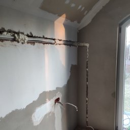 ADEK - Wnętrze w trakcie prac wykończeniowych: widoczne przewody elektryczne w peszlach, zabezpieczone pianką montażową w bruzdach ściany, puszka elektryczna z wystającymi przewodami, fragment ściany...