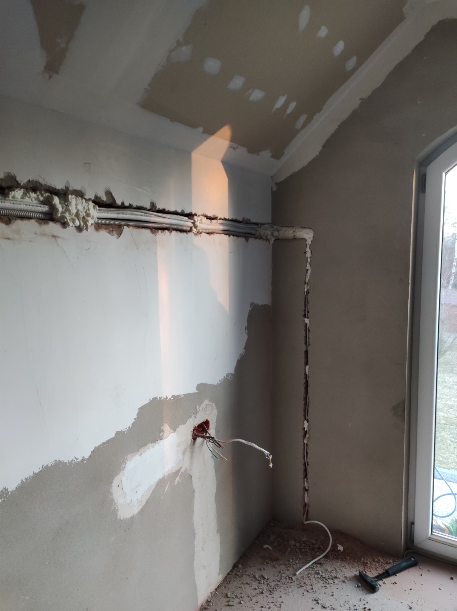 Wnętrze w trakcie prac wykończeniowych: widoczne przewody elektryczne w peszlach, zabezpieczone pianką montażową w bruzdach ściany, puszka elektryczna z wystającymi przewodami, fragment ściany...