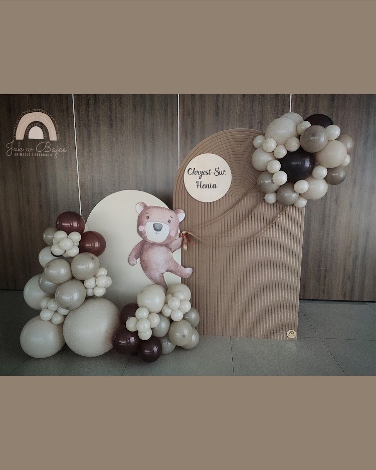 Dekoracja na chrzest: beżowe balony, drewniane panele, postać misia z kokardą i tabliczka z napisem 'Chrzest Św. Henia'.