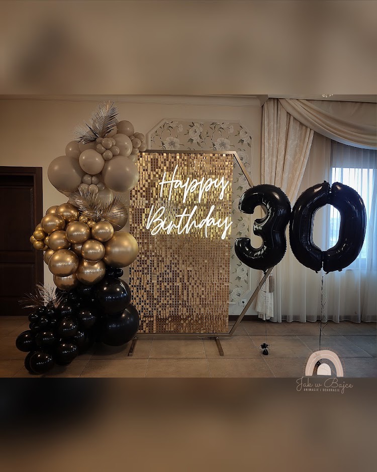 Dekoracja urodzinowa z balonów w odcieniach złota, beżu i czerni, z błyszczącym złotym tłem i neonowym napisem 'Happy Birthday', oraz balonami w kształcie cyfry 30.