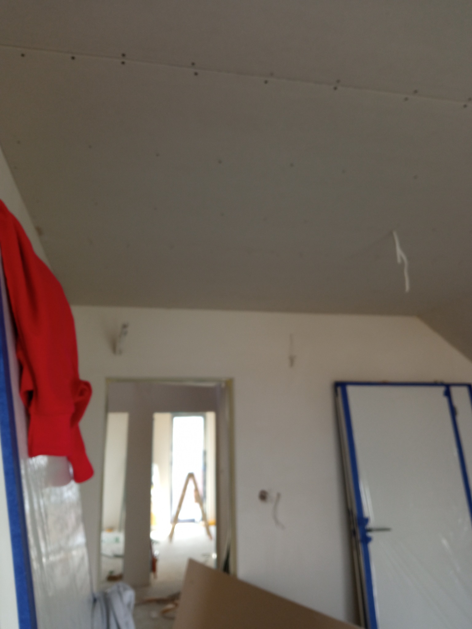 Montaż płyt kartonowo-gipsowych na suficie, widoczne łączenia i śruby, w tle drzwi i drabina malarska.