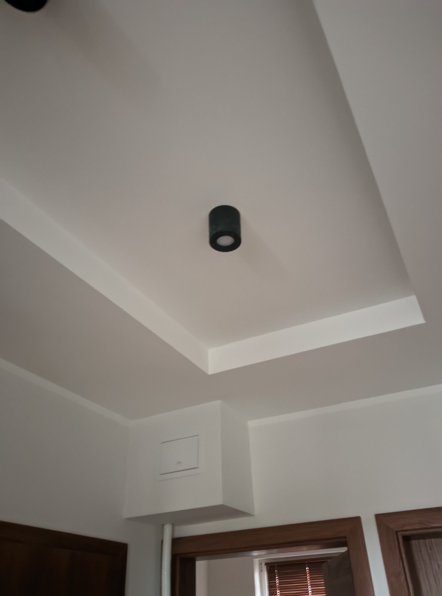 Biały sufit z czarnym punktowym oświetleniem LED, widoczne fragmenty ścian i drzwi z drewnianymi framugami.