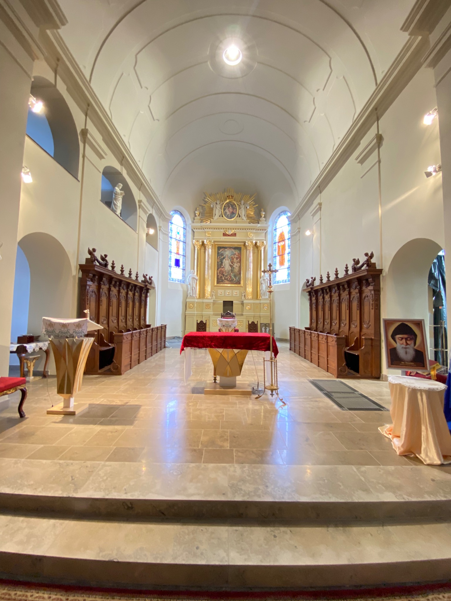 Wnętrze kościoła z drewnianymi stallami, ołtarzem z czerwonym obrusem i witrażami. Widok na odnowioną posadzkę i sklepienie. Prace konserwatorskie w zabytkowym obiekcie sakralnym.