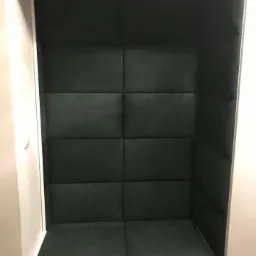 Wnęka z tapicerowanym siedziskiem i ścianą w kolorze ciemnej zieleni, podzielona na równe kwadraty, wbudowana w białą zabudowę.