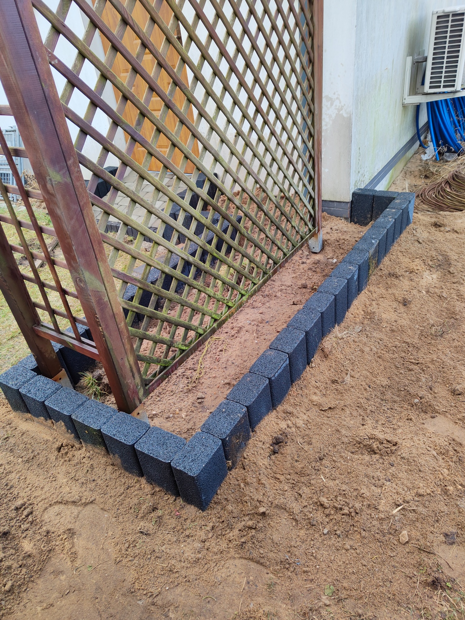 Przygotowanie rabaty we Włocławku: obrzeże z ciemnej kostki ułożone wzdłuż drewnianej kratownicy, ziemia przygotowana pod nasadzenia.