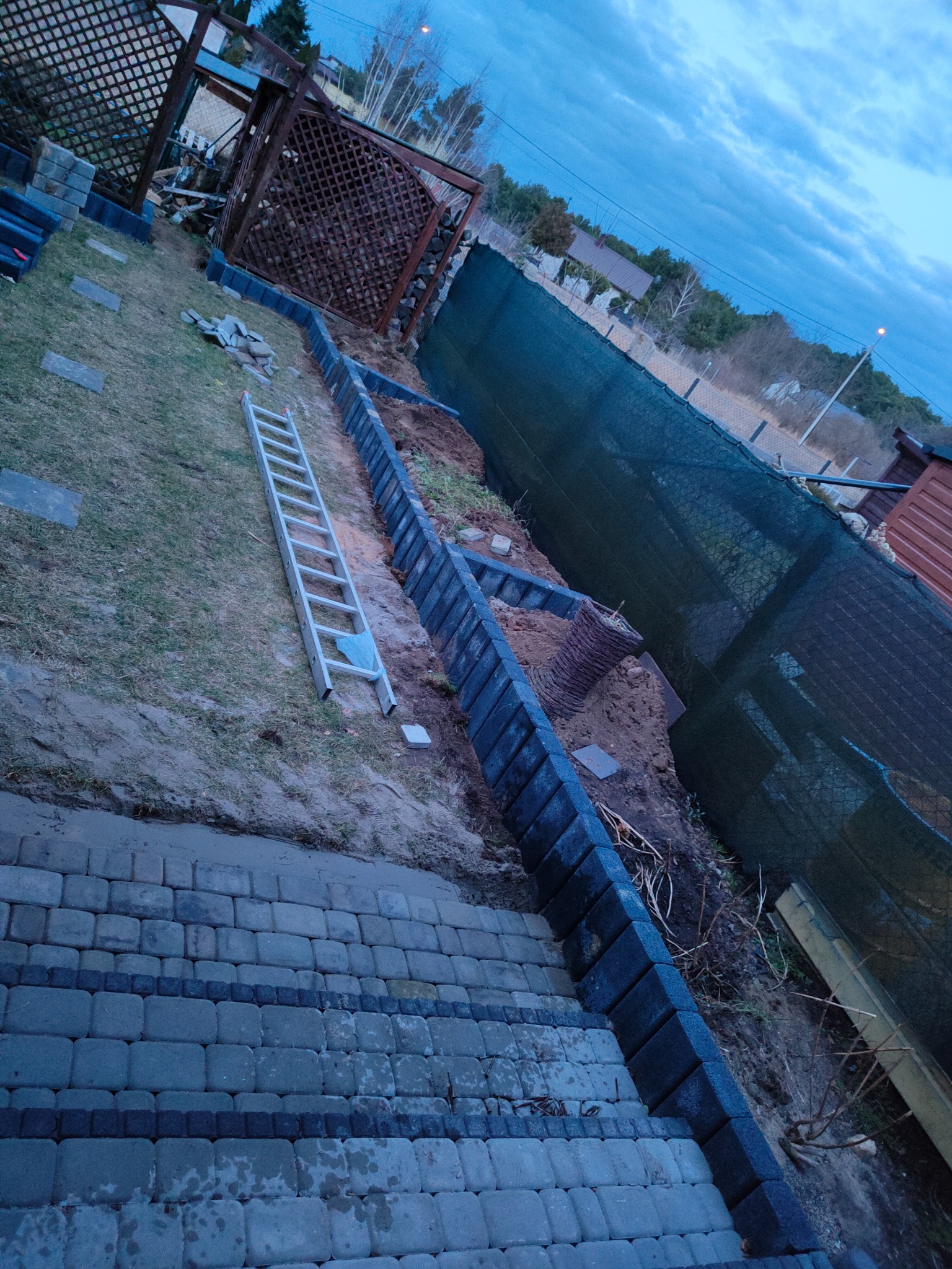 Prace przygotowawcze do aranżacji ogrodu: ułożona kostka brukowa, wytyczone rabaty z obrzeżami, drabina oparta o teren budowy, widok z góry na posesję.