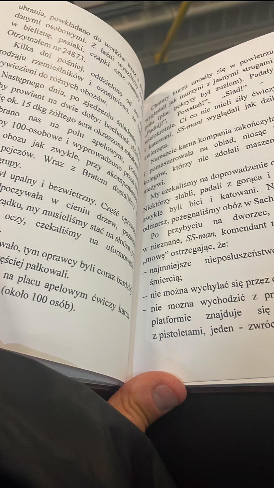 Otwarta książka z tekstem w języku polskim, widoczny fragment palca trzymającego stronę, tekst o tematyce obozowej.