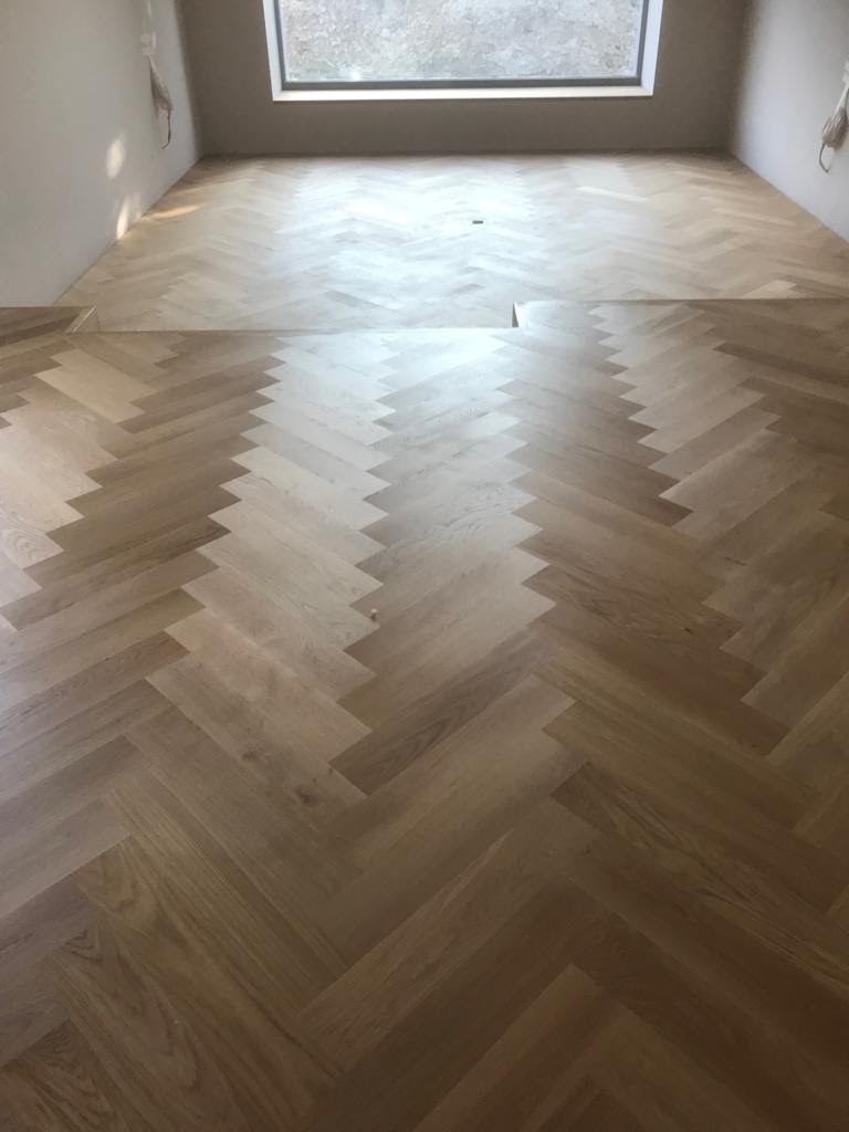 Nowa, jasna podłoga z parkietu ułożonego we wzór jodełki francuskiej w Damnicy, widoczny fragment niedokończonego montażu przy ścianie.