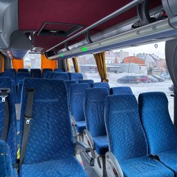 Przewozy „Yellon Bus”' Sławomir Jelonek - Wnętrze autobusu z niebieskimi siedzeniami w kropki, widok na zasłonięte okna i zimowy krajobraz za nimi. Pasy bezpieczeństwa na fotelach.