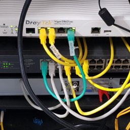 P.H.U ANDRZEJ GRZESIAK - Panel krosowniczy z routerem DrayTek Vigor2862Lac, switchem TP-Link T1600G-28PS i licznymi kablami Ethernet oznaczonymi etykietami, w szafie rack.