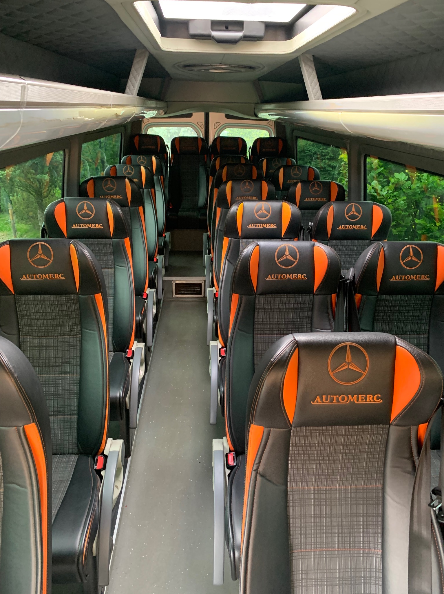 Wnętrze luksusowego busa z czarno-pomarańczowymi skórzanymi fotelami z logo firmy Automec, widok na pełny rząd siedzeń.