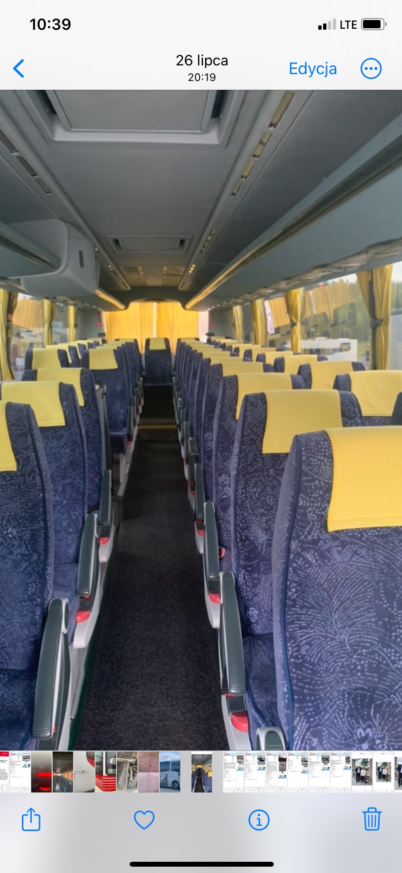 Wnętrze autobusu z rzędami niebieskich siedzeń z żółtymi zagłówkami, widok na korytarz w kierunku okna z żółtymi zasłonami.