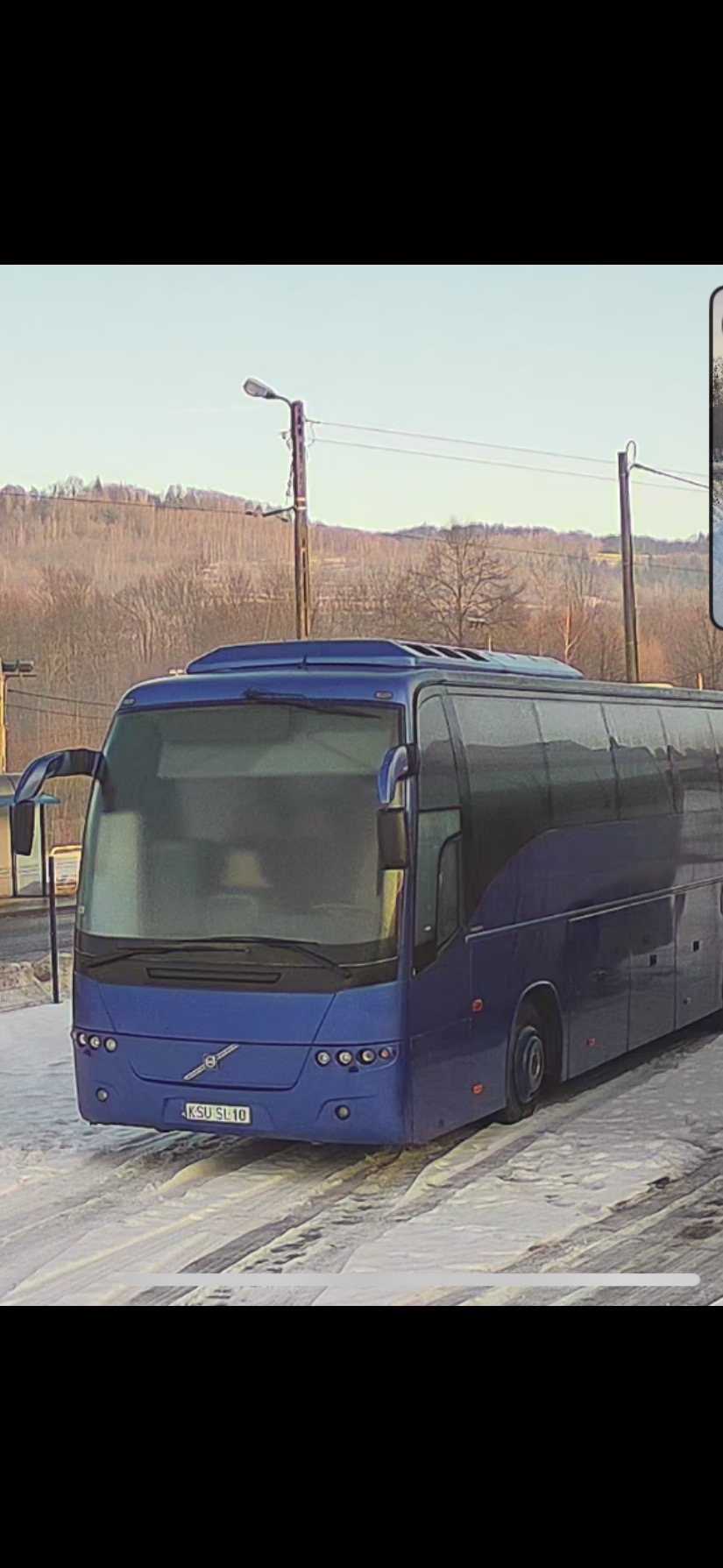 Niebieski autokar Volvo na tle zimowego krajobrazu w Bieńkówce. Widoczny zarys gór i słup oświetleniowy. Autobus czeka na klientów.