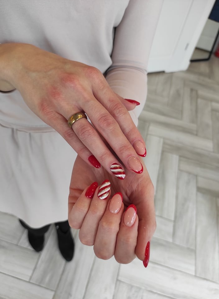 Dłonie z manicure hybrydowym: klasyczny french z czerwoną końcówką oraz paznokieć akcentowy w biało-złote paski, dodatkowo złoty pierścionek na palcu wskazującym.