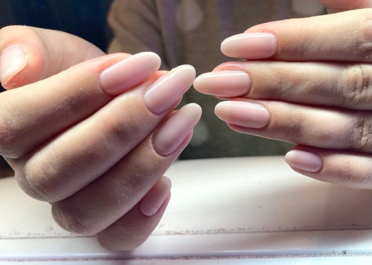 Delikatny, mlecznoróżowy manicure hybrydowy na dłoniach, zbliżenie na owalne paznokcie o gładkiej powierzchni.