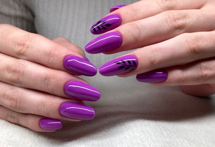 Dłonie z fioletowymi paznokciami w kształcie migdała, dwa z nich ozdobione czarnym motywem roślinnym.