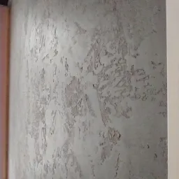 Szara elewacja wewnętrzna z efektem dekoracyjnym imitującym łuszczący się tynk, widoczna z bliska.