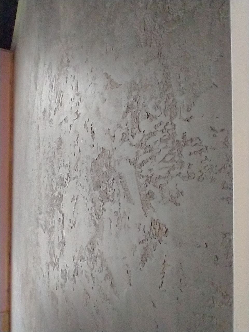 Szara elewacja wewnętrzna z efektem dekoracyjnym imitującym łuszczący się tynk, widoczna z bliska.