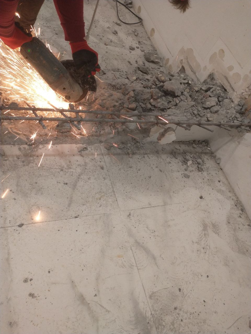 Demontaż zbrojenia w betonie za pomocą szlifierki kątowej, iskry i gruz na posadzce z płytek.
