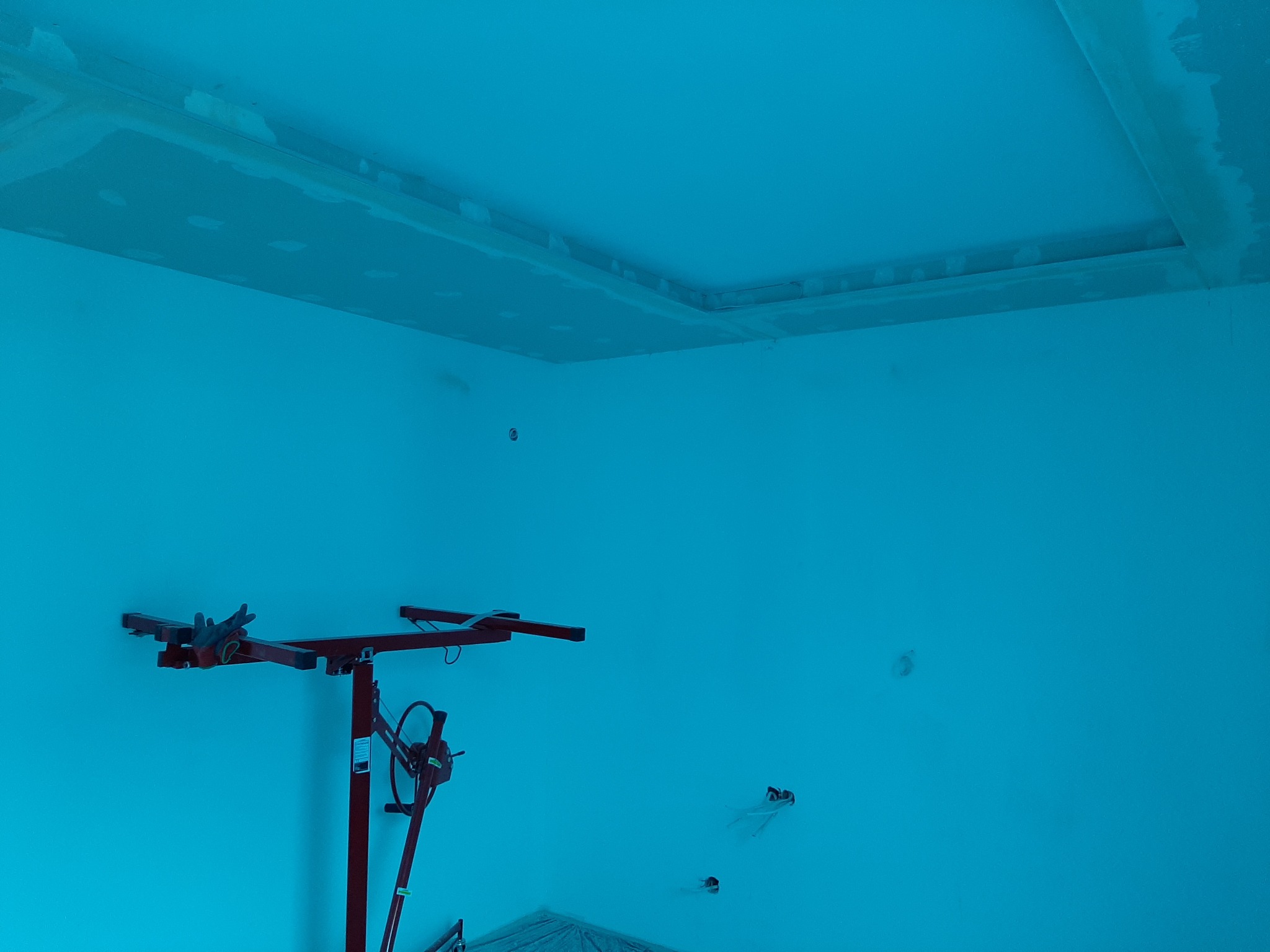 Montaż sufitu podwieszanego z płyt kartonowo-gipsowych; widoczny podnośnik do płyt i częściowo zamaskowane łączenia płyt.