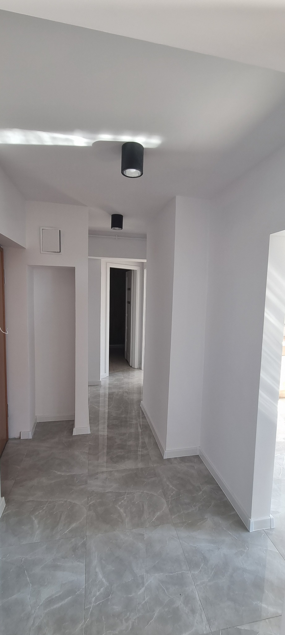 Wnętrze korytarza po remoncie z szarą marmurkową podłogą, białymi ścianami i czarnymi lampami sufitowymi.