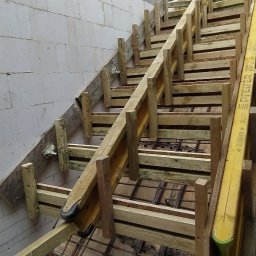 BiałoBud - Szczegółowe ujęcie szalunku schodów z widocznym zbrojeniem, przylegającego do ściany z betonu komórkowego.