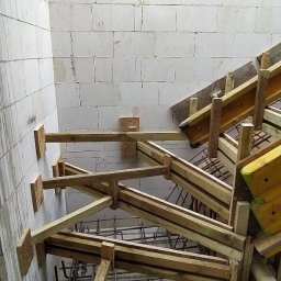 BiałoBud - Szczegółowy widok z góry na szalunek drewniany z widocznym zbrojeniem stalowym, przygotowany do zalania betonem, na tle ściany z bloczków betonowych i surowego stropu.