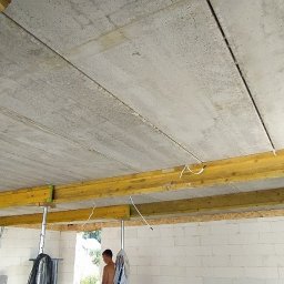 BiałoBud - Szare płyty stropowe żelbetowe podparte żółtymi belkami na metalowych stemplach w surowym stanie budynku z białego bloczka.