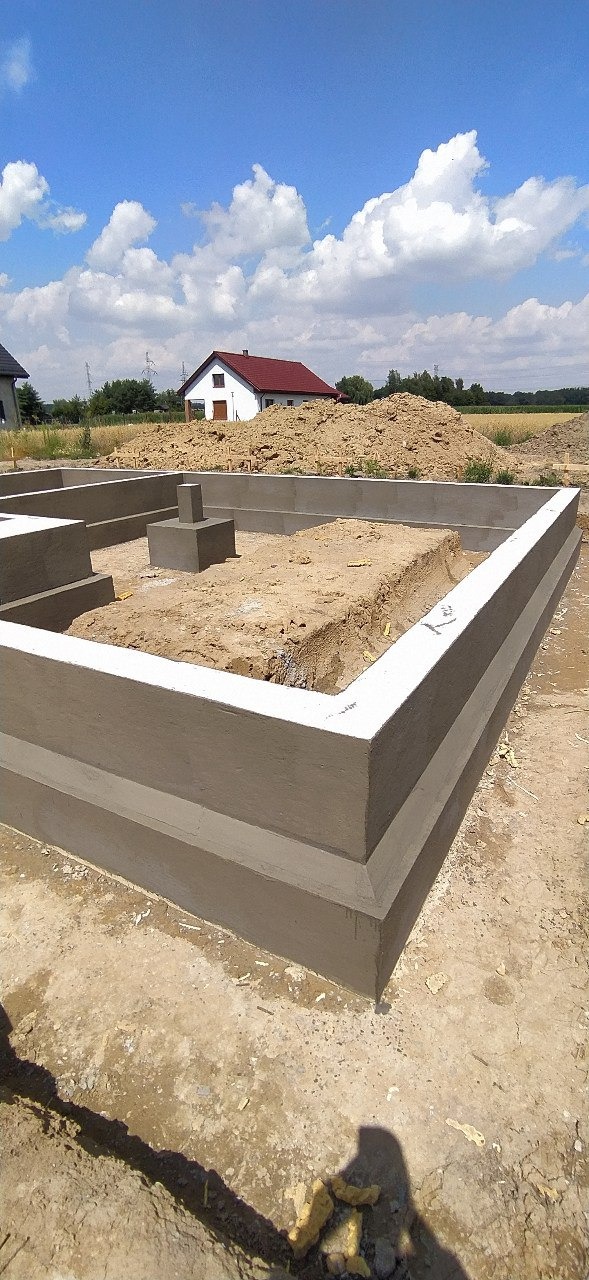 Świeżo wylane, wypoziomowane i otynkowane fundamenty pod budowę domu jednorodzinnego, widok z poziomu gruntu w słoneczny dzień.