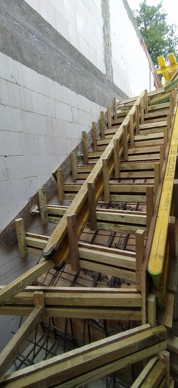 Szczegółowe ujęcie szalunku schodów z widocznym zbrojeniem, przylegającego do ściany z betonu komórkowego.