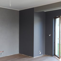Ah-Pro - Wnętrze pokoju po malowaniu ścian na szaro i grafitowo, widoczne fragmenty instalacji elektrycznej, podłoga wyłożona panelami.