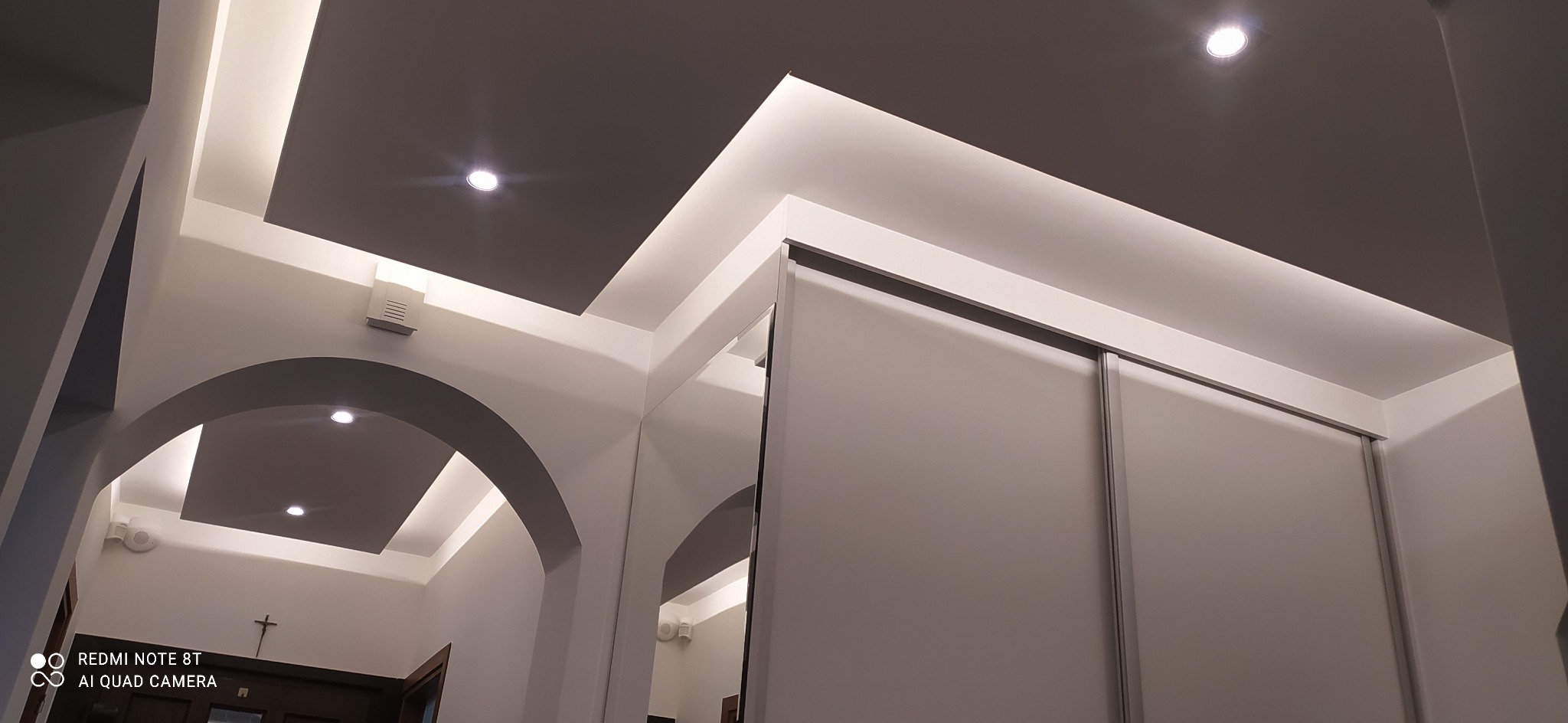 Nowoczesne wnętrze mieszkania z podwieszanym sufitem z oświetleniem LED, łukowym przejściem i szafą wnękową z przesuwnymi drzwiami.