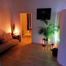 A&P Atelier Beauty Massage - Przytulne wnętrze gabinetu z sofą, stolikiem z dekoracjami, rośliną w doniczce i świecami, w tle widoczny stół do masażu.