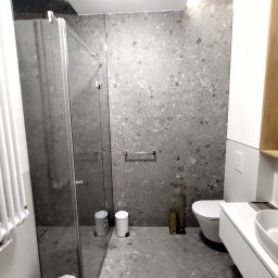 Remys - Nowoczesna łazienka z szarymi płytkami lastryko na ścianach i podłodze. Kabina prysznicowa ze szklanymi drzwiami, biała umywalka z szafką i toaleta.