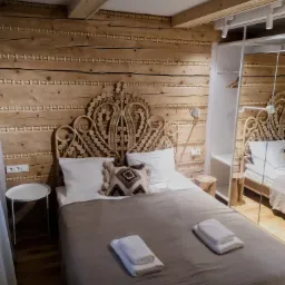 Drewniana sypialnia w góralskim stylu z dekoracyjną ścianą, łóżkiem z wiklinowym zagłówkiem i nowoczesną szafą z lustrem.