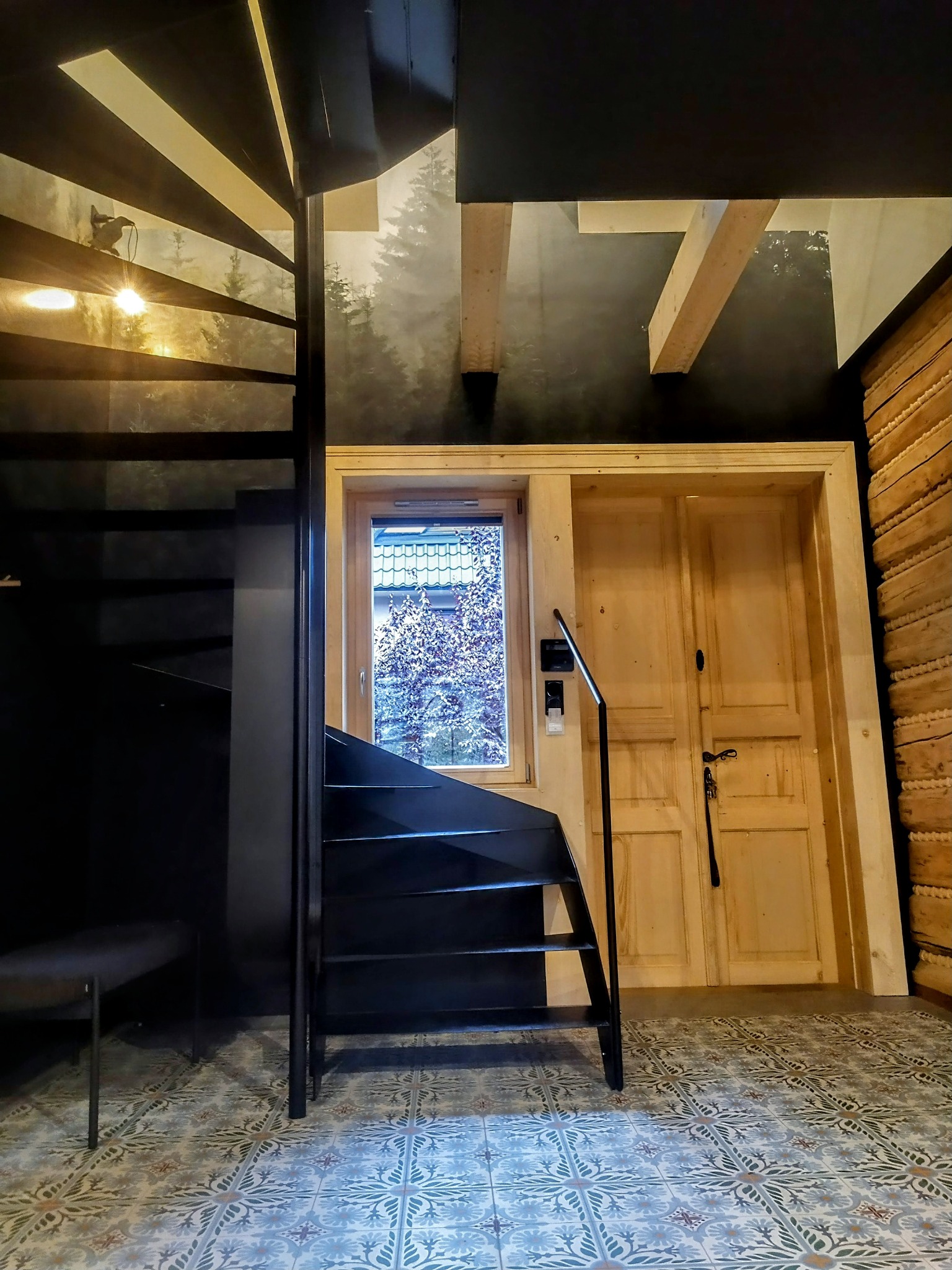 Wnętrze z drewnianymi drzwiami i spiralnymi schodami na tle ściany z motywem lasu. Dekoracyjne płytki podłogowe. Widok z okna na drzewo.