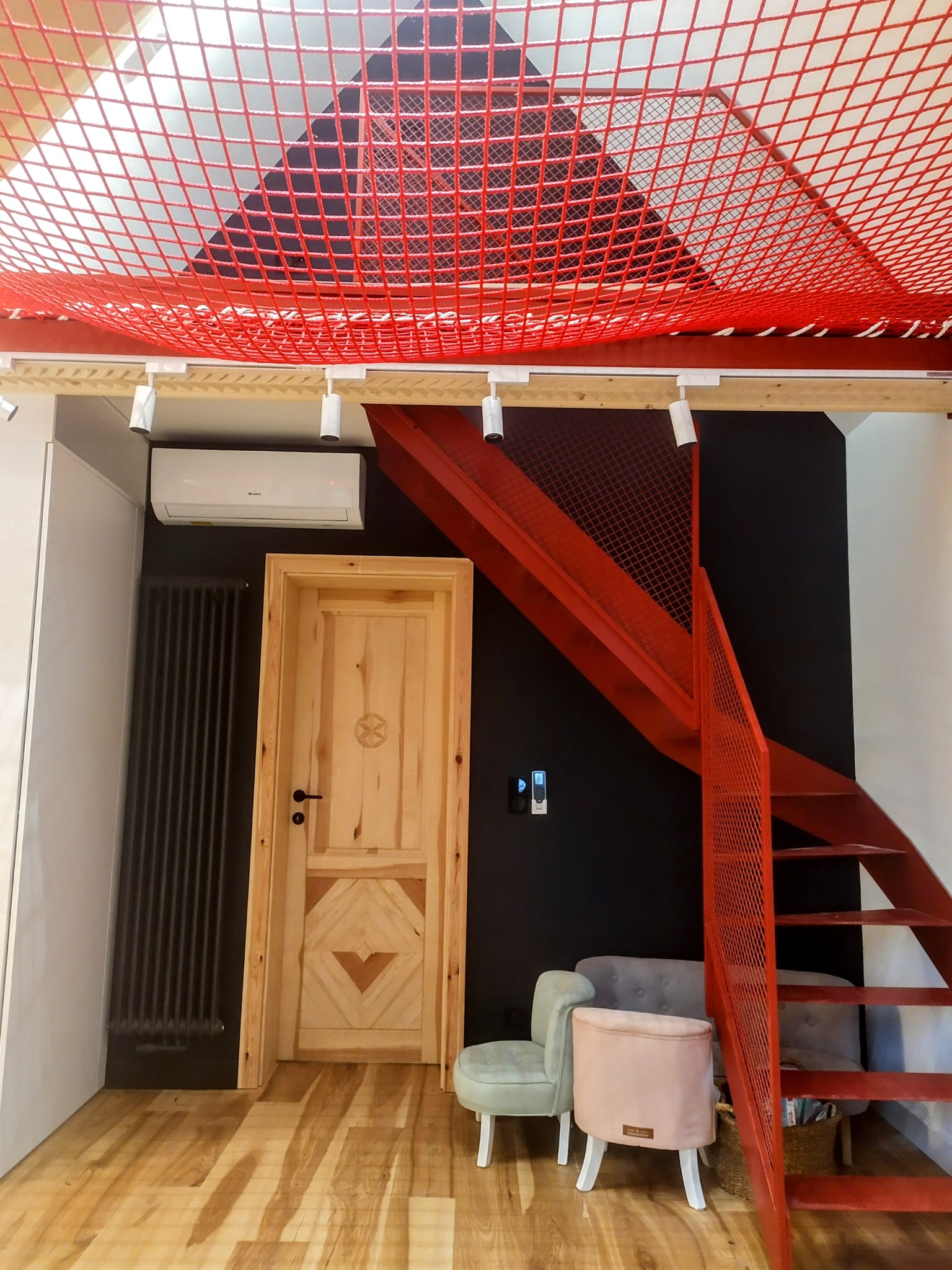 Wykończenie wnętrza z drewnianymi akcentami w Limanowej: czerwona siatka sufitowa, schody, drzwi z wzorem, grzejnik i klimatyzacja na czarnej ścianie.