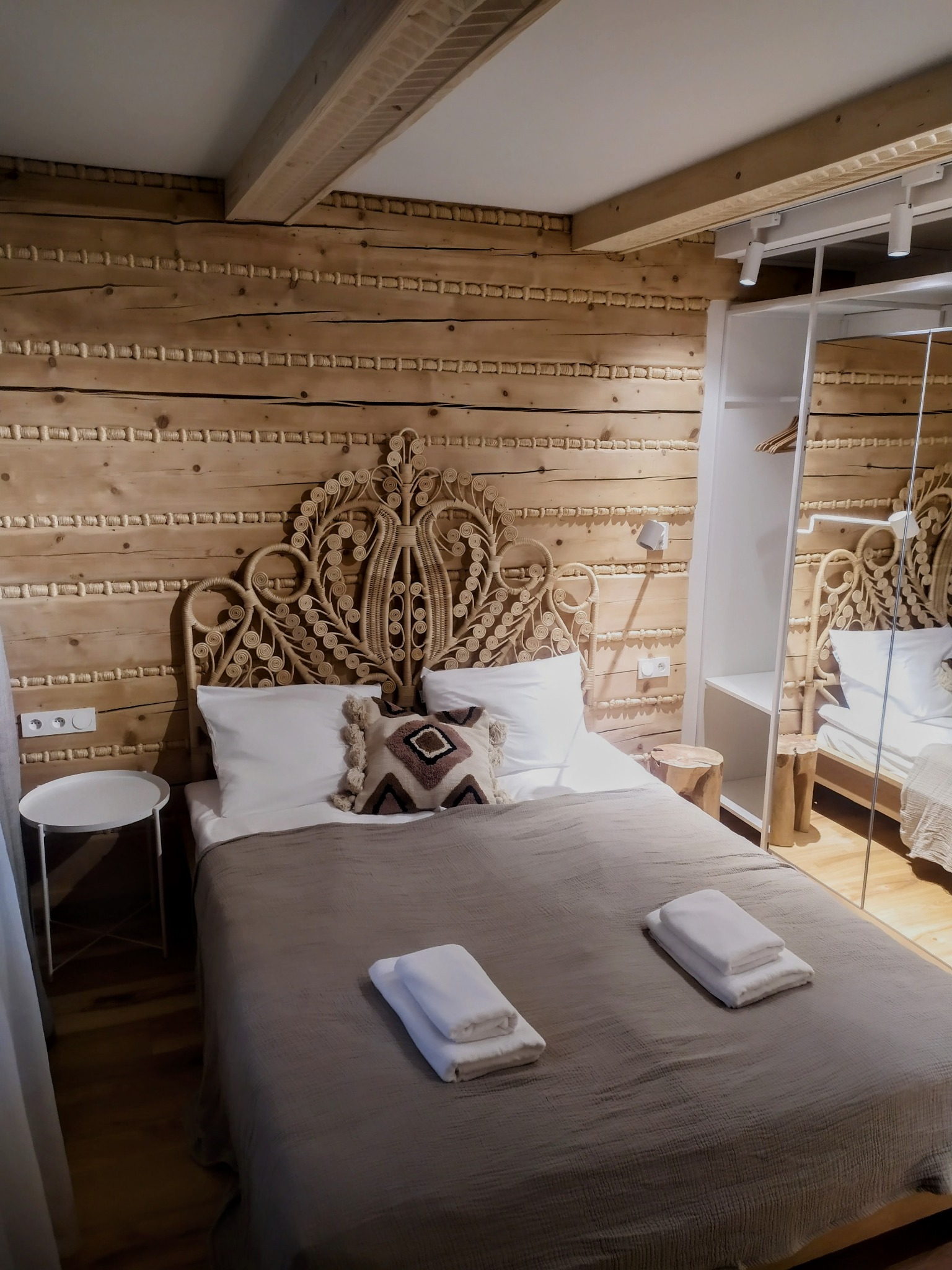 Drewniana sypialnia w góralskim stylu z dekoracyjną ścianą, łóżkiem z wiklinowym zagłówkiem i nowoczesną szafą z lustrem.