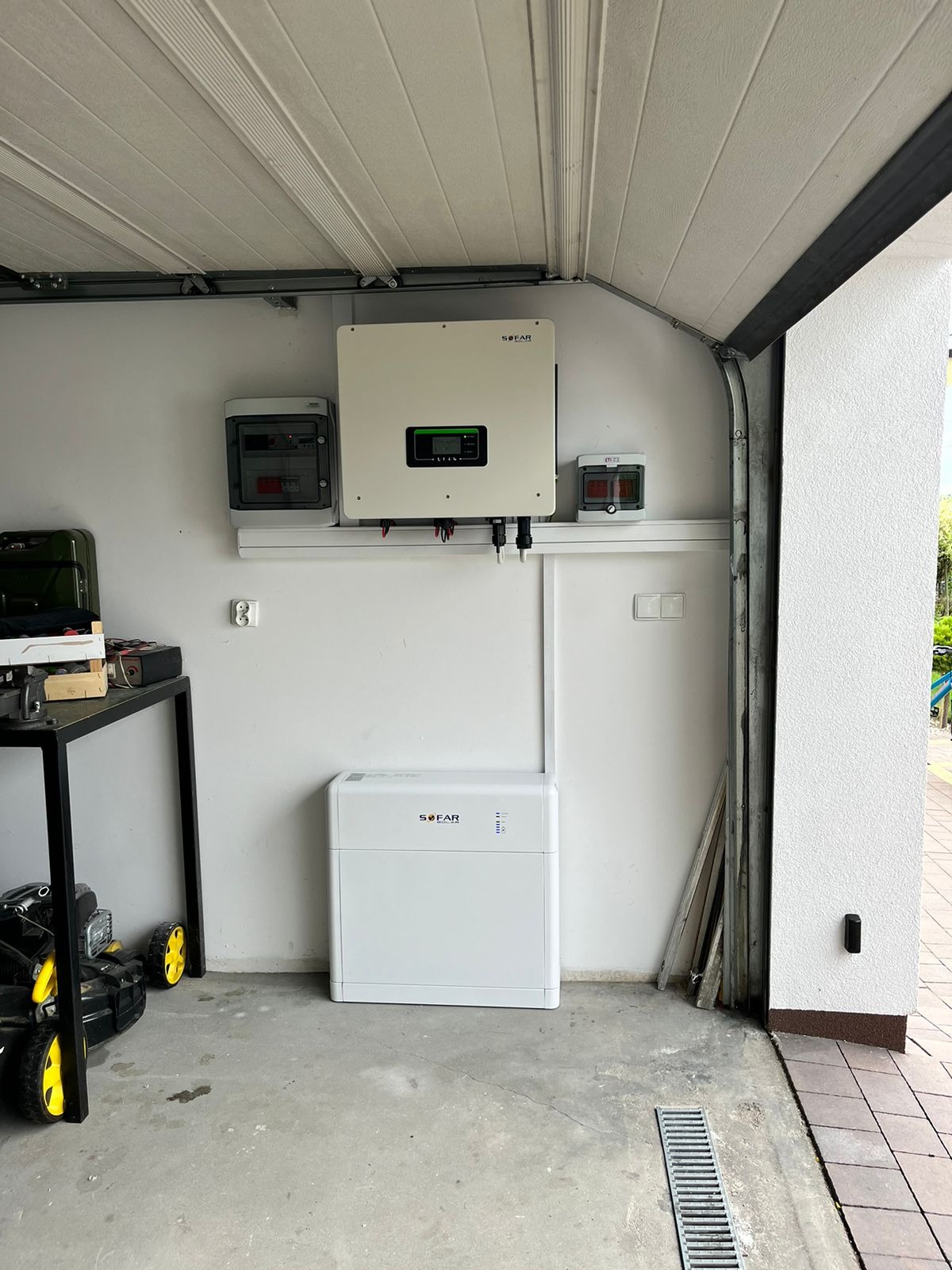 Biały magazyn energii SOFAR i falownik zamontowane w garażu na tle białej ściany, widoczna skrzynka elektryczna i fragment bramy garażowej.