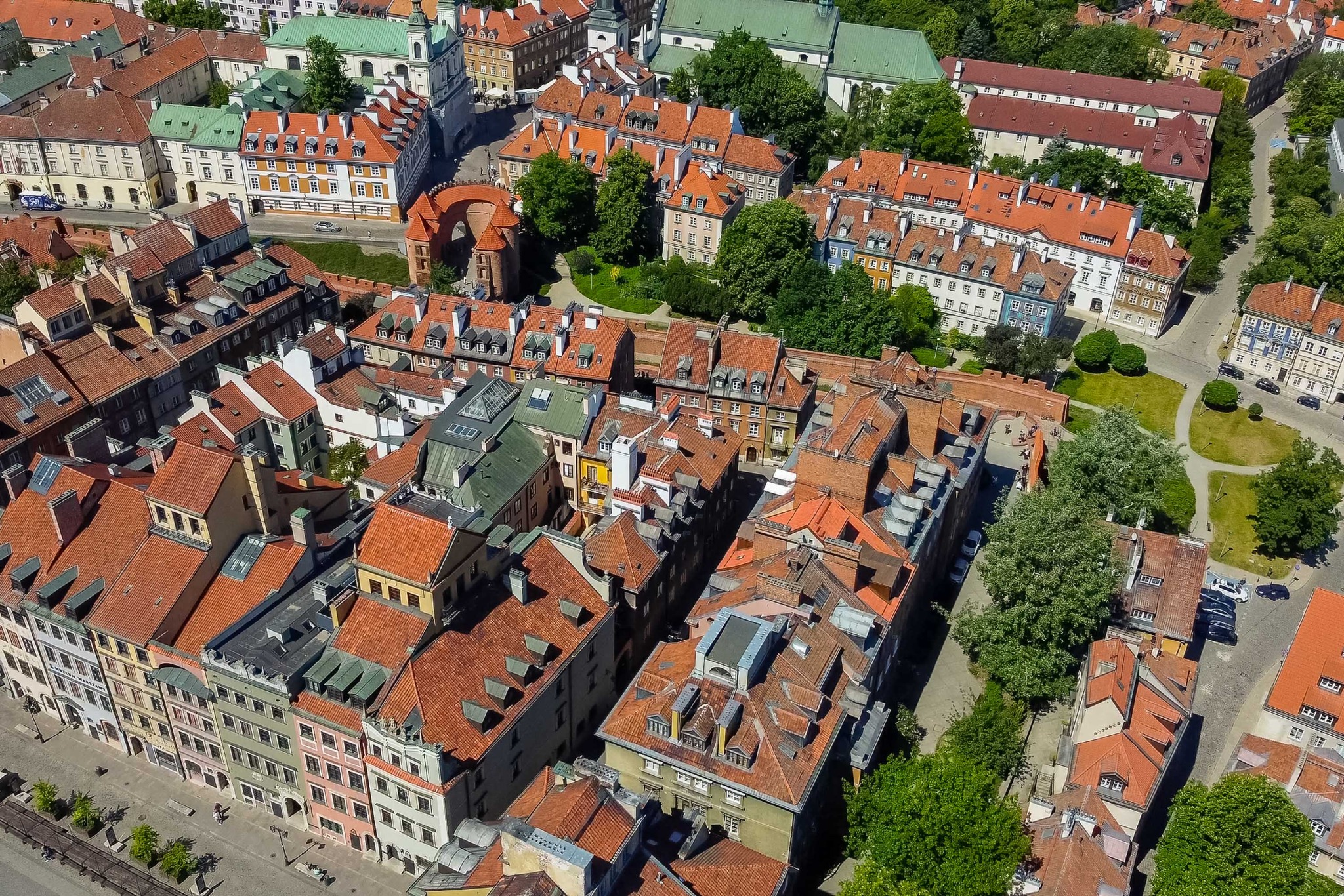 Panorama Starego Miasta w Warszawie z lotu ptaka, ukazująca charakterystyczne czerwone dachy kamienic, zieleń drzew i zabytkową architekturę w słoneczny dzień.