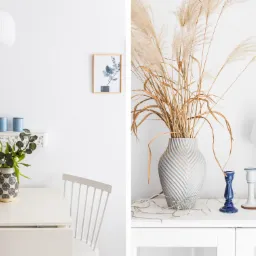 Jasne wnętrze z dekoracjami: bukiet tulipanów w ozdobnym wazonie na stole, suszone trawy w wazonie o wzorze chevron, ceramiczne świeczniki i lampka nocna na komodzie, obrazek z motywem roślinnym...