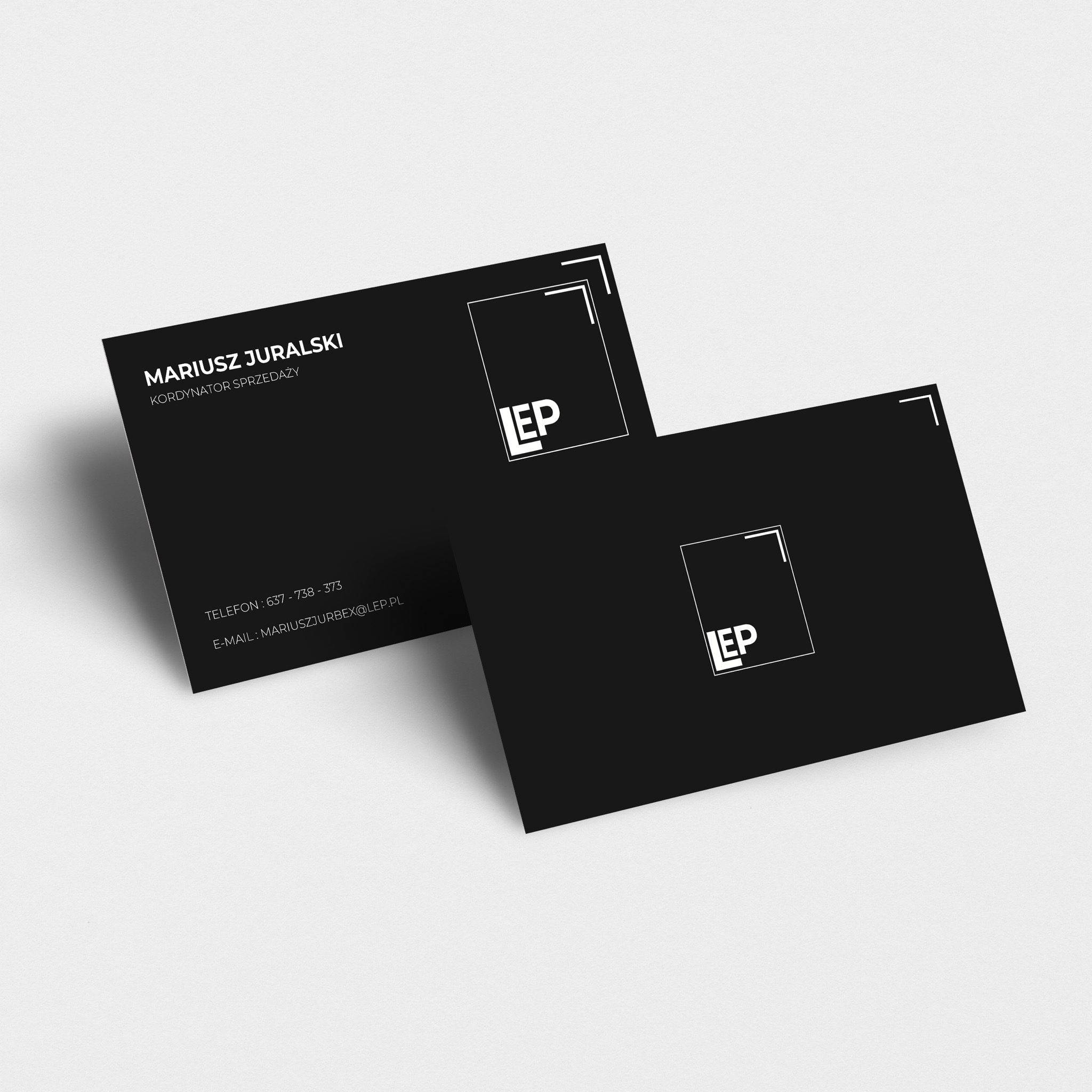 Dwie czarne wizytówki z białym logo i danymi kontaktowymi, leżące na jasnym tle pod lekkim kątem.