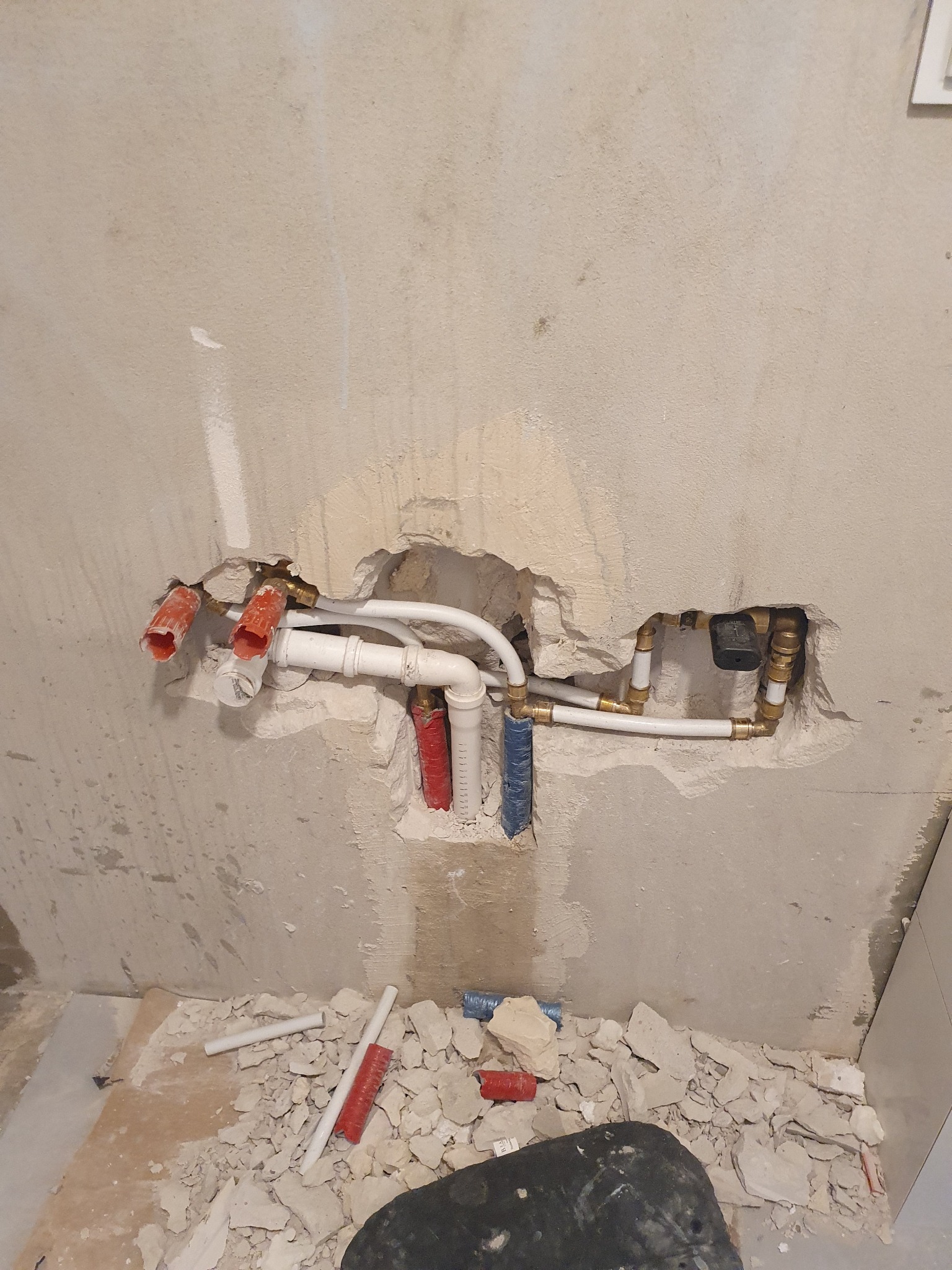 Odsłonięte rury wodne i kanalizacyjne w ścianie podczas prac instalacyjnych w pomieszczeniu, gruz na podłodze.