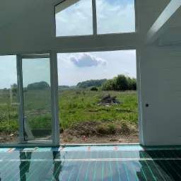 Montaż maty grzewczej w nowo budowanym domu z widokiem na łąkę przez duże okna.