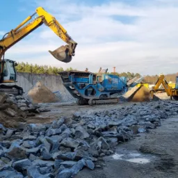 Żółta koparka Liebherr, niebieski przesiewacz Terex Pegson i koparko-ładowarka JCB podczas prac ziemnych na placu z gruzem i piaskiem, w tle drzewa i błękitne niebo.