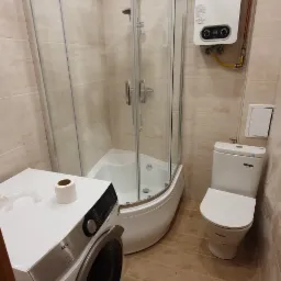 Wykończona łazienka z kabiną prysznicową narożną, pralką AEG i piecykiem Junkers, wykończona płytkami imitującymi drewno