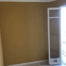 Pokój po malowaniu ścian na musztardowy kolor, widoczna biała listwa przypodłogowa, fragment okna i płytek podłogowych.