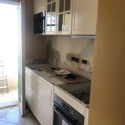 NewTomorrowHome - Białe szafki kuchenne w trakcie montażu w Radomiu, widoczne niedoskonałości ściany przed wykończeniem.