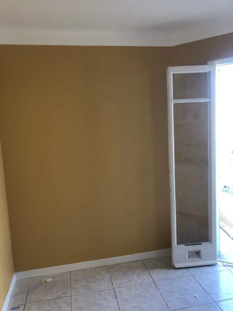 Pokój po malowaniu ścian na musztardowy kolor, widoczna biała listwa przypodłogowa, fragment okna i płytek podłogowych.